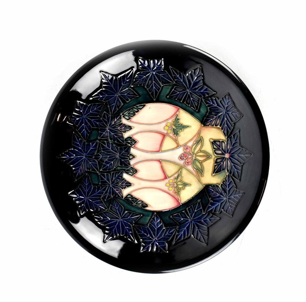 A Moorcroft plate, indigo ground with holly and ivy pattern, green marks to base, diameter 26cm.