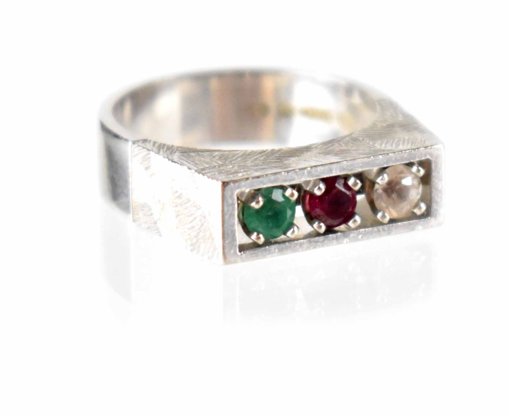 A 1970s modern 18ct white gold ring, channel set with a diamond, ruby and emerald,