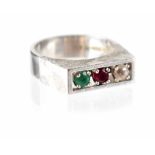 A 1970s modern 18ct white gold ring, channel set with a diamond, ruby and emerald,