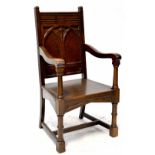 A Gothic Revival oak open elbow chair with carved panel back on a plank seat,