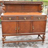 An early 20th century oak sideboard with carved back above three drawers and three doors on turned