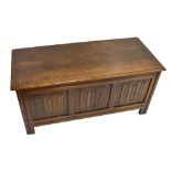 A reproduction oak blanket box with hinged lid above carved panel front, 105 x 46cm.