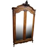 A large French walnut armoire with carved pediment above two full length bevelled mirror doors,