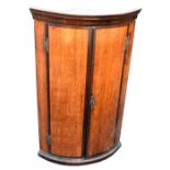 A Georgian oak and mahogany crossbanded two door wall hanging bowfronted corner cupboard with H-