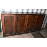 A large stained pitch pine cupboard with two pairs of panel doors enclosing shelves and pigeonholes,