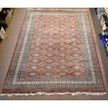 A large hand knotted woolen Bokhara-type carpet with geometric medallions on a peach ground, 382 x