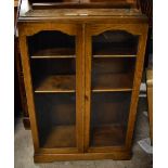 An oak bookcase with twin glazed doors enclosing three shelves, height 107cm, width 68cm, depth