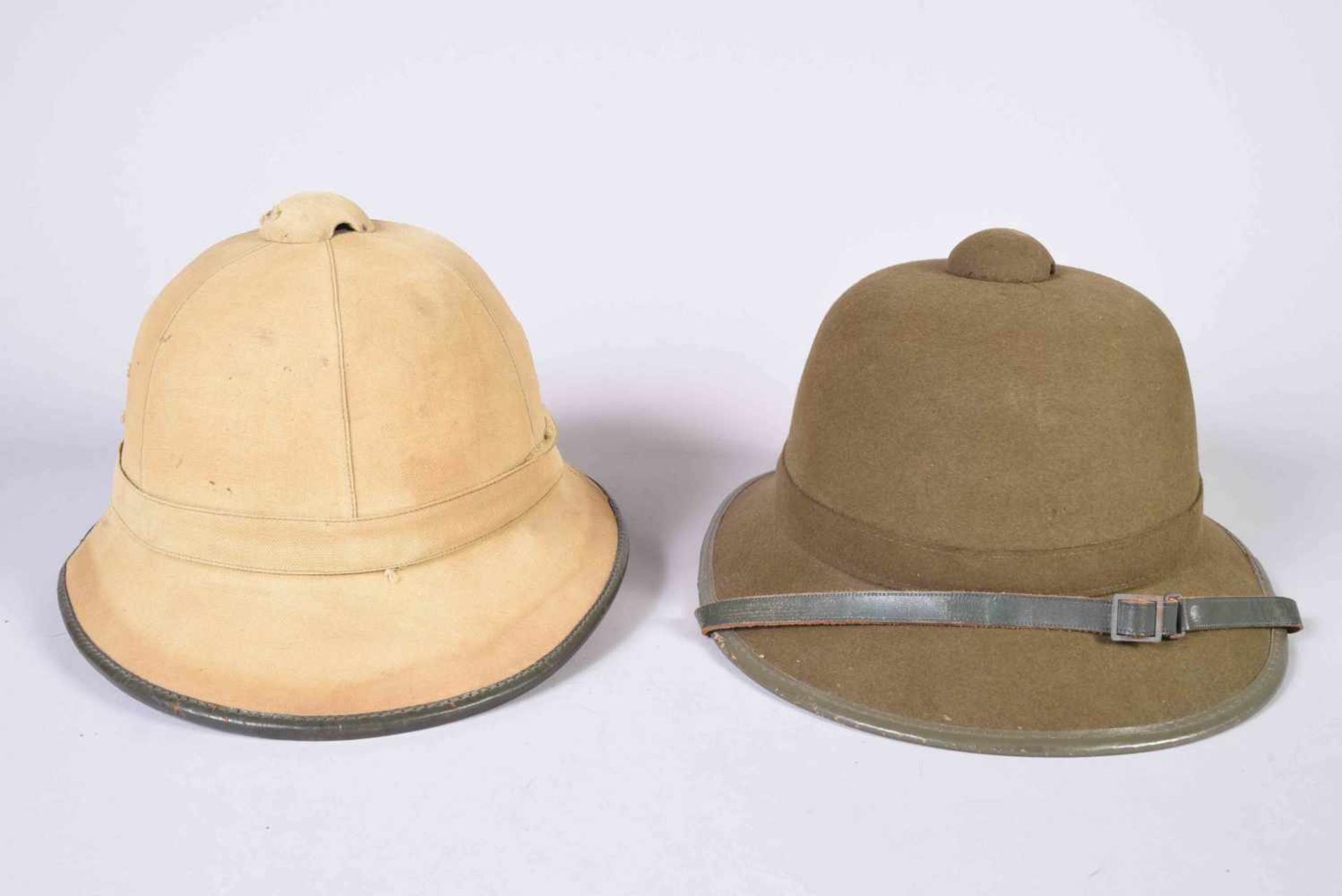2 casques coloniaux de l’Afrika Korps. L’un en liège recouvert de toile beige avec galon de cuir