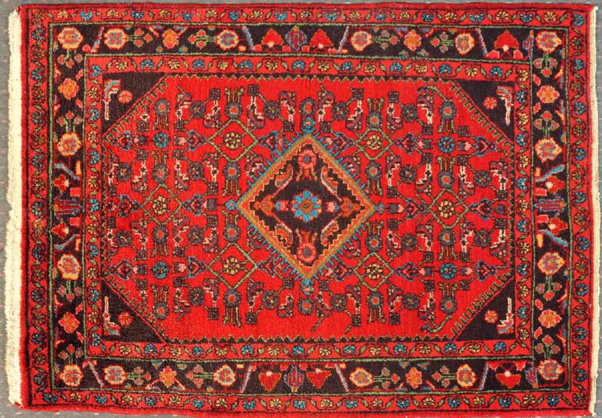 Hamadan, Persien, 112 x 156 cmWolle, rotgrundig, mehrfarb. Rautenmittelstück, umgeben von stilis.