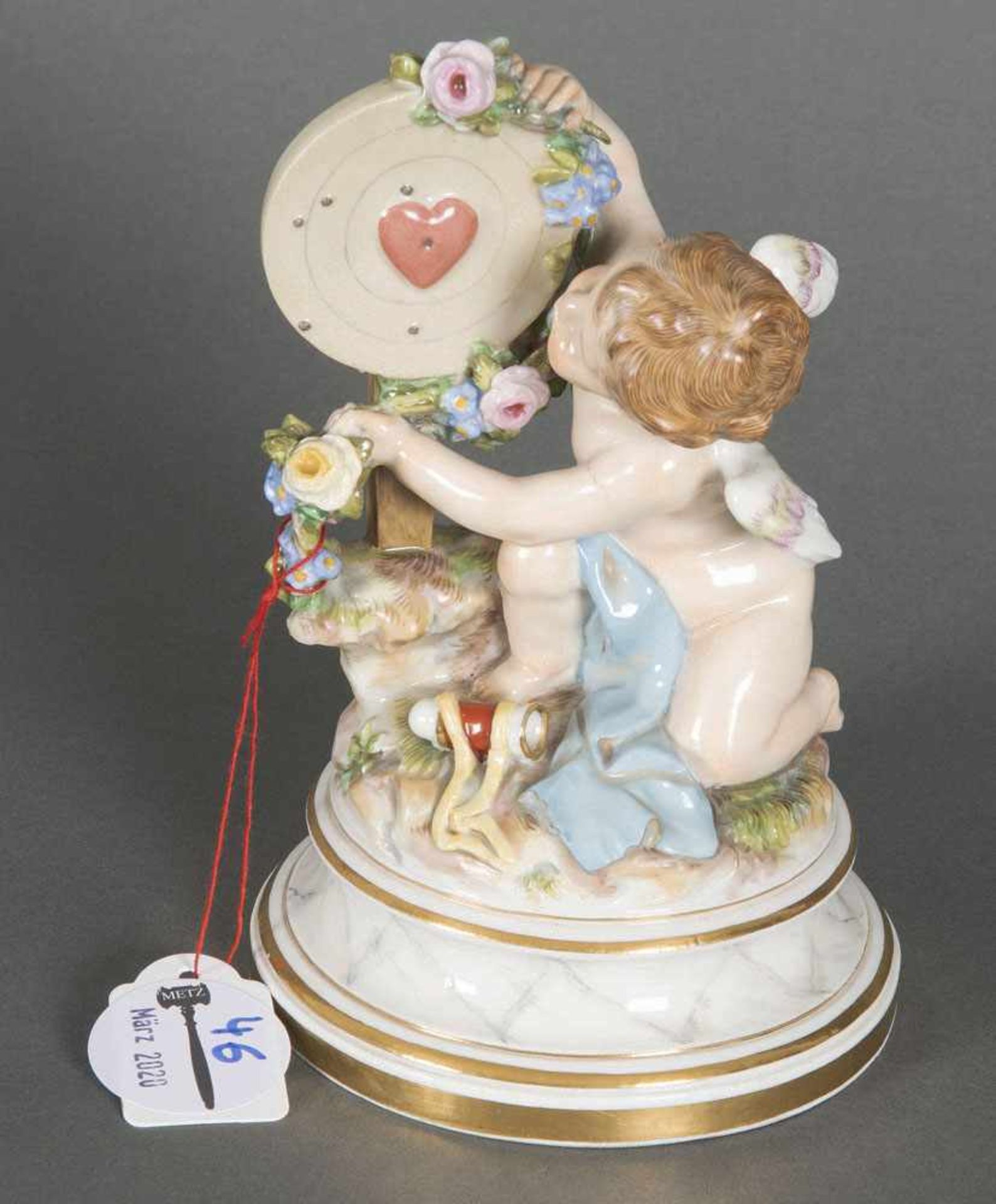 Kniender Putto. Meissen 19. Jh. Mit Schießscheibe und Herz, umgeben von Blumengirlanden.