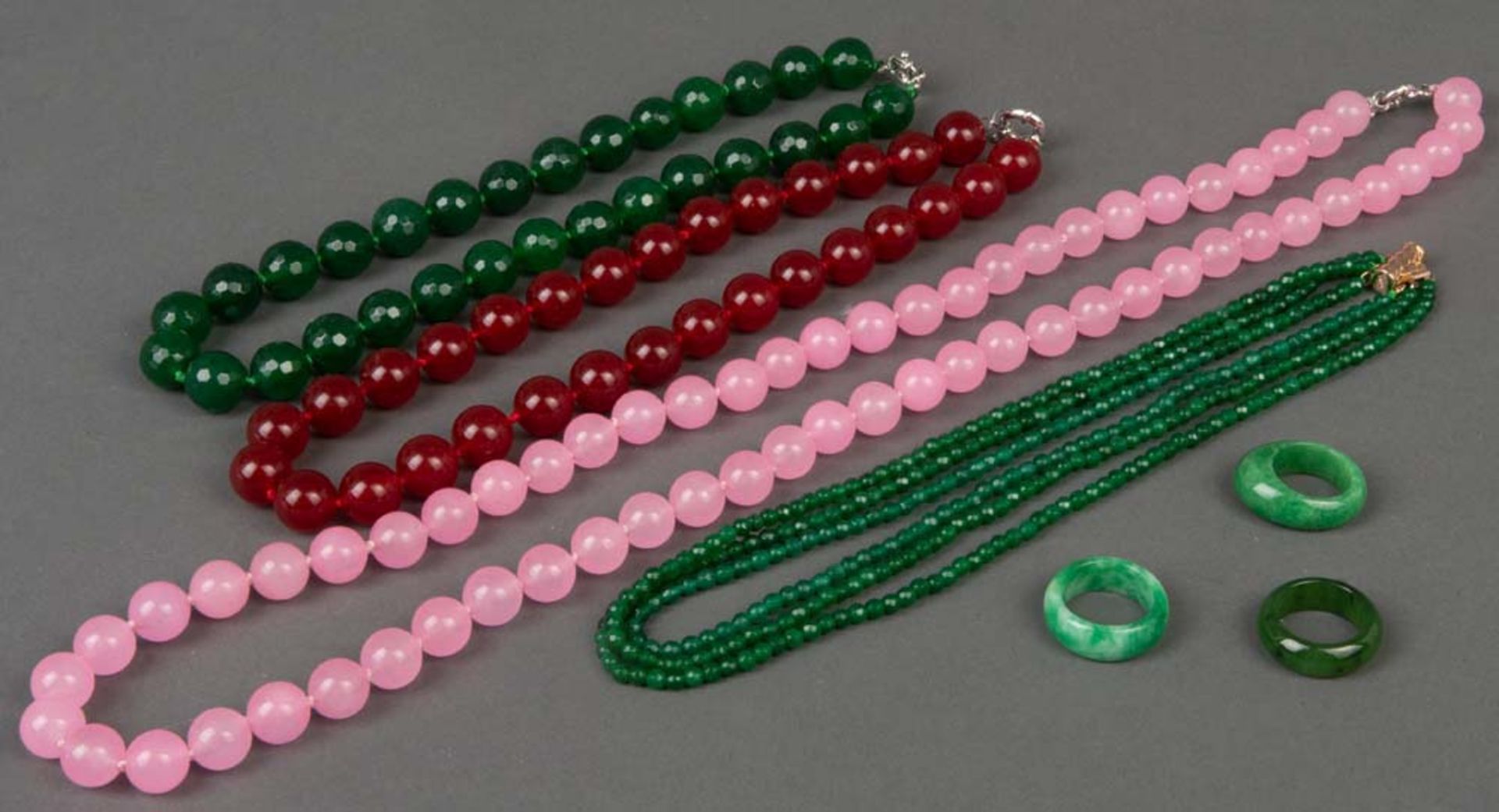 Vier Halsketten mit karneol-, jade- und rosafarbenen Kugeln (L=43 bis 80 cm) sowie drei Jade-Ringe.