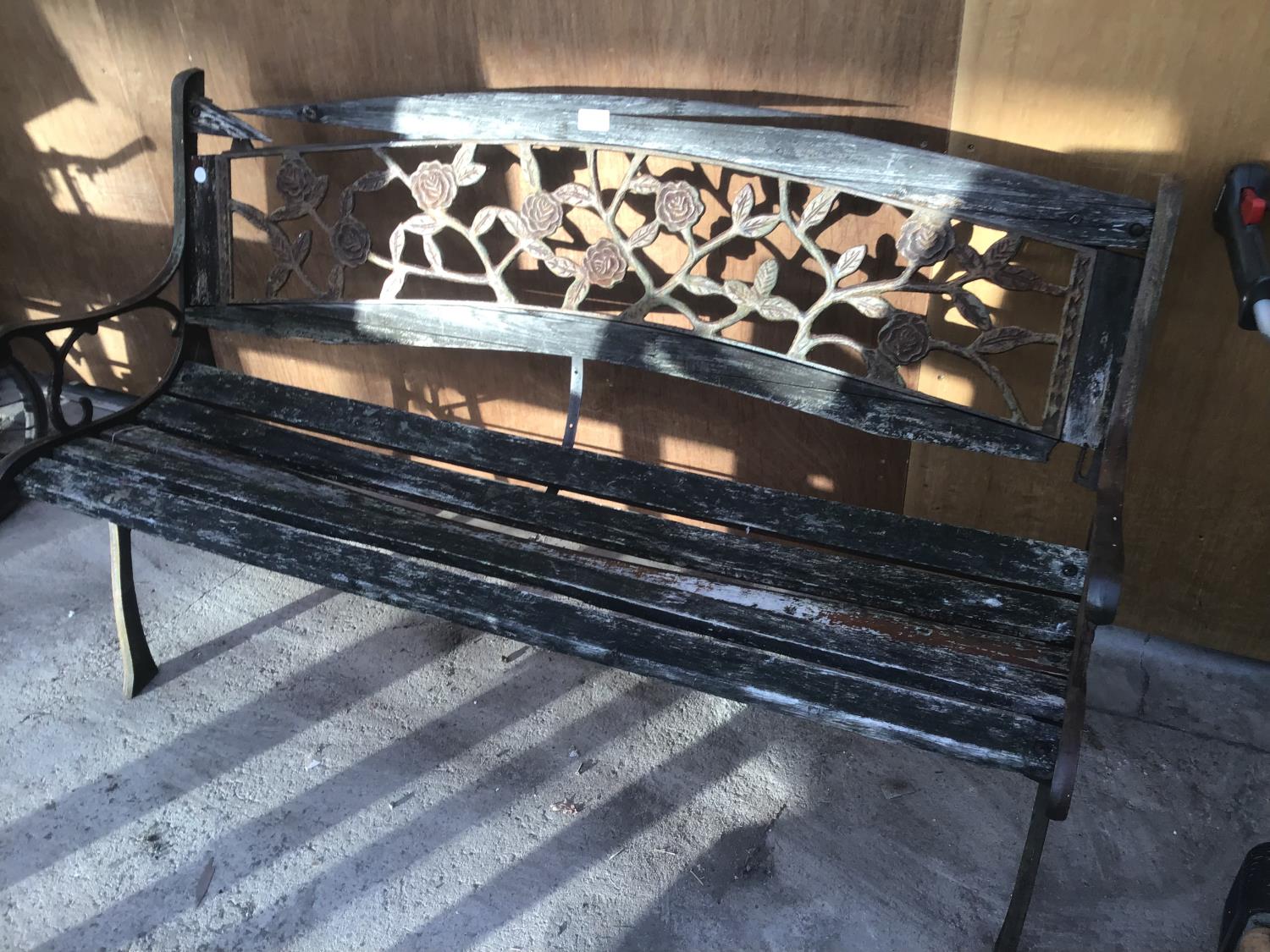 A WOODEN BENCH WITH CAST IRON ENDS AND A CAST IRON ROSE DESIGN BACK