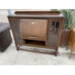 AN ART DECO STYLE OAK SIDE BY SIDE CABINET WITH FALL FRONT, ONE DRAWER AND TWO GLAZED PANEL SIDE