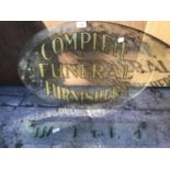 AN OVAL GLASS SIGN PAINTED WITH 'COMPLETE FUNERAL FURNISHERS' AND A FURTHER GLASS HANGING PLAQUE (