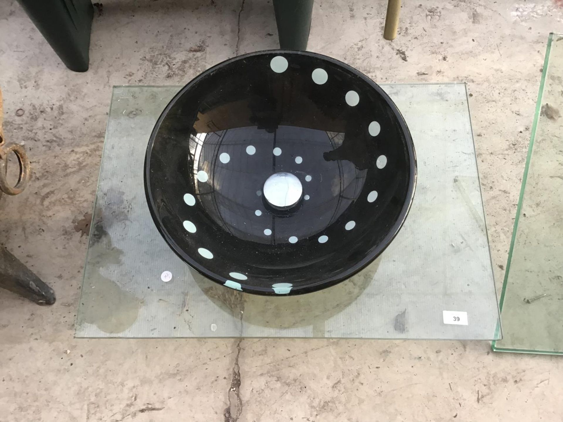 A BLACK GLASS ORNATE BASIN ON A GLASS TOP