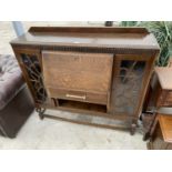 AN ART DECO STYLE OAK SIDE BY SIDE CABINET WITH FALL FRONT, ONE DRAWER AND TWO GLAZED PANEL SIDE