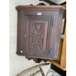 A SMALL WALL MOUNTED OAK CORNER CABINET WITH CARVED PANEL DOOR