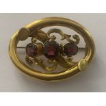 A YELLOW METAL PINCHBECK BROOCH SET WITH THREE GARNETS