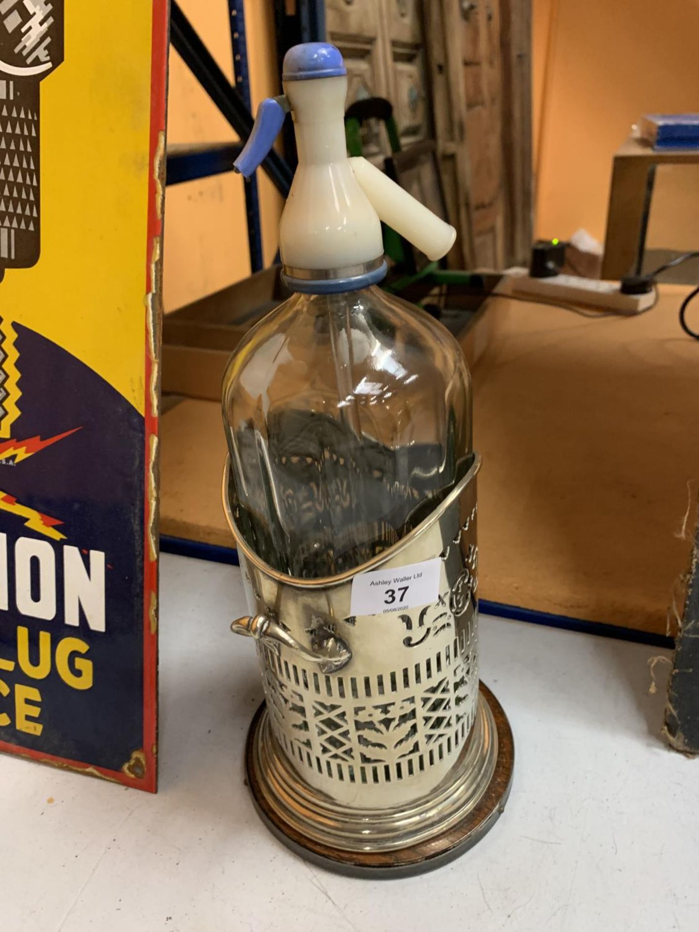 A VINTAGE SODA SYPHON IN AN ORNATE PLATE HOLDER ON A WOODEN BASE