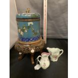 A LARGE ORIENTAL CLOISONNE LIDDED JAR ON AN ORNATE CARVED WOODEN STAND AND TWO SMALL JUGS