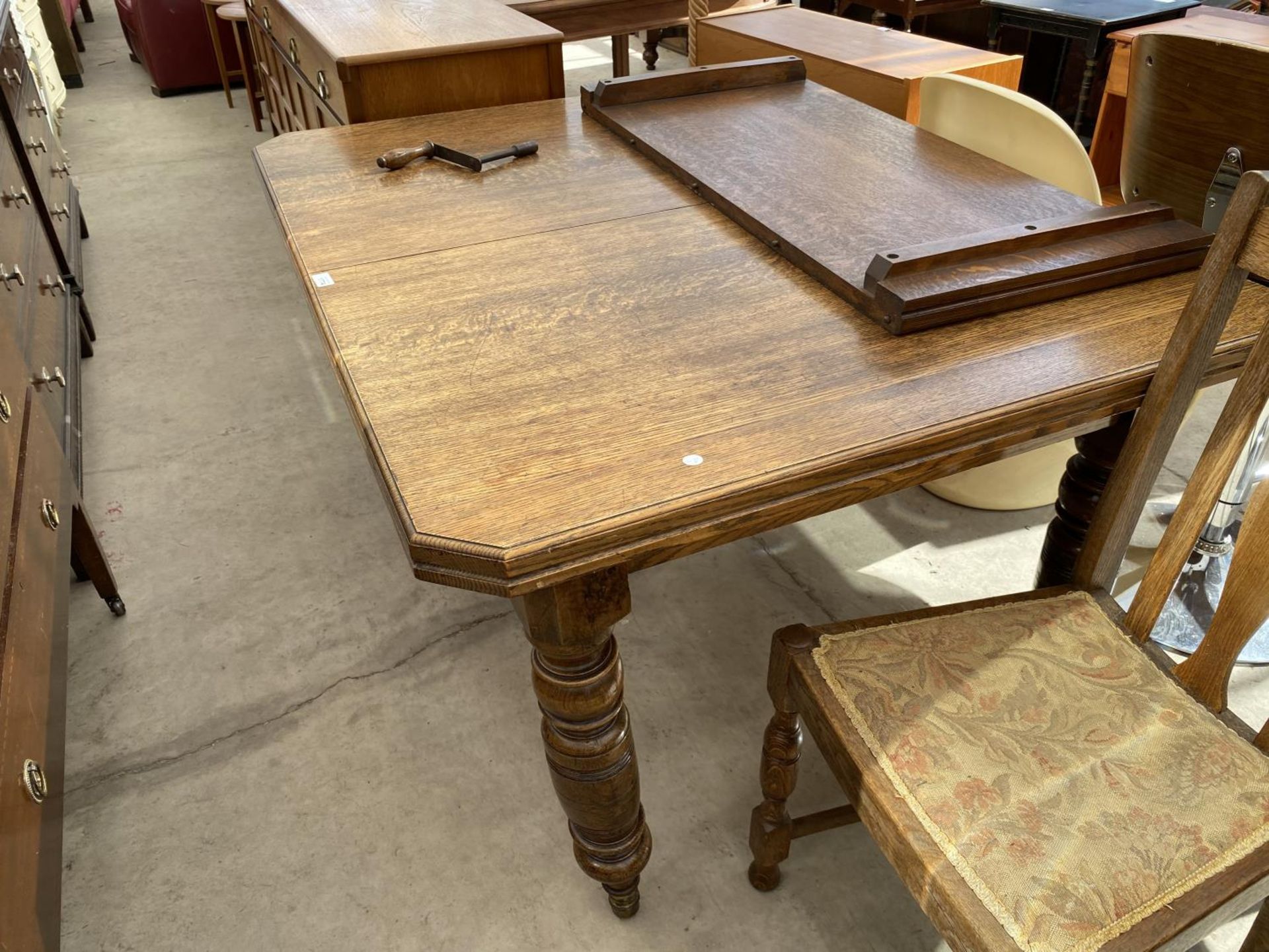 AN EDWARDIAN OAK WIND OUT DINING TABLE WITH CANTED CORNERS, SPARE LEAF AND WINDER 53 INCHES X 42