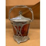 A CRANBERRY GLASS JAR WITH ORNATE METAL SURROUND WITH LID AND HANDLE ATTACHED