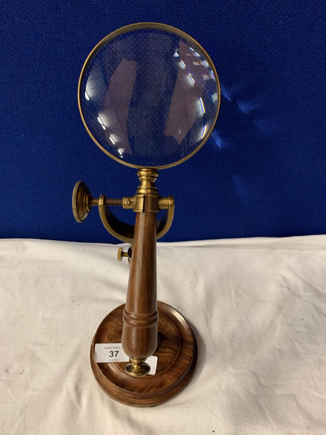 A VINTAGE BRASS MAGNIFTING GLASS ON A WOOD AND BRASS STAND