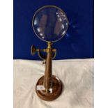 A VINTAGE BRASS MAGNIFTING GLASS ON A WOOD AND BRASS STAND