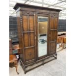 AN EARLY 20TH CENTURY OAK JACOBEAN STYLE THREE DOOR WARDROBE WITH CENTRAL MIRROR, ON TURNED OPEN
