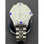 A LADIES FASHION WATCH WITH ORNATE CLEAR AND BLUE STONE DECORATION ON A WHITE METAL STRAP