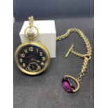 A PLATED POCKET WATCH ON A CHAIN WITH A PURPLE STONE FOB