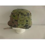 A GREEN PAINTED GERMAN HELMET WITH CAMOUFLAGE COVER