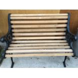 A TWO SEATER SLATTED GARDEN BENCH WITH CAST IRON BENCH ENDS