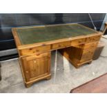 A MODERN PINE KNEEHOLE DESK ENCLOSING FIVE DRAWERS AND ONE CUPBOARD, HAVING INSET LEATHER TOP,