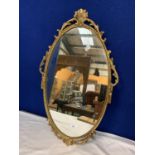 AN OVAL ORNAMENTAL GILT METAL FRAMED MIRROR