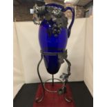 A BLUE GLASS URN ON A DECORATIVE METAL TRIPOD BASE