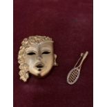 TWO SILVER GILT BROOCHES, ONE A TENNIS RACKET, THE OTHER A MASK