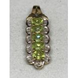 A 9 CARAT GOLD PENDANT WITH FIVE IN LINE PALE GREEN STONES SURROUNDED BY CLEAR STONE CHIPS