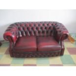 An oxblood red leather button backed two seater chesterfield sofa