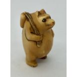 A signed netsuke of a bear on hind legs carrying a wine container over it's shoulder
