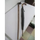 A wooden walking stick with handle in the form of an elephant along with an umbrella