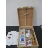 A wooden artist box with assorted contents including paint, brushes, canvas etc