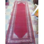 An Eastern hand woven red ground runner - length 320cm, width 110cm