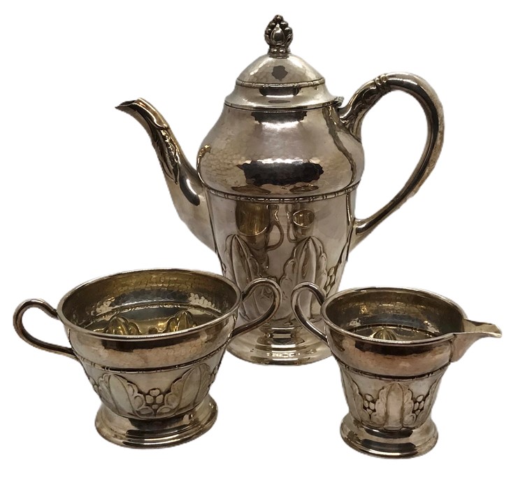 An Arts and Crafts silver plated coffee pot, sugar bowl, and cream jug with hammered detailing,