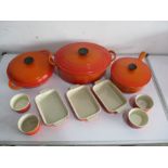 A collection of Le Creuset in orange, including saucepans, dishes, ramakins etc
