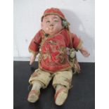 An antique doll depicting a Chinese man in red cotton smock with silk trousers- approx 20cm height