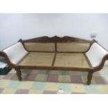A teak plantation daybed with twin strolling arms and cane seat and back.