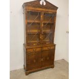 A reproduction walnut wood glazed display bookcase over cupboard.