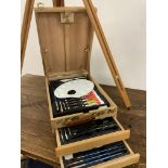 An artists easel and an equipment box with contents.