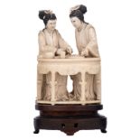 A Chinese ivory carved group, depicting two ladies playing a board game, on a matching wooden base w